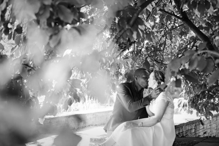 braut und Bräutigam sitzen am Hochzeitstag unter einem schattigen baum in der sonne und genießen einen zärtlichen Moment.